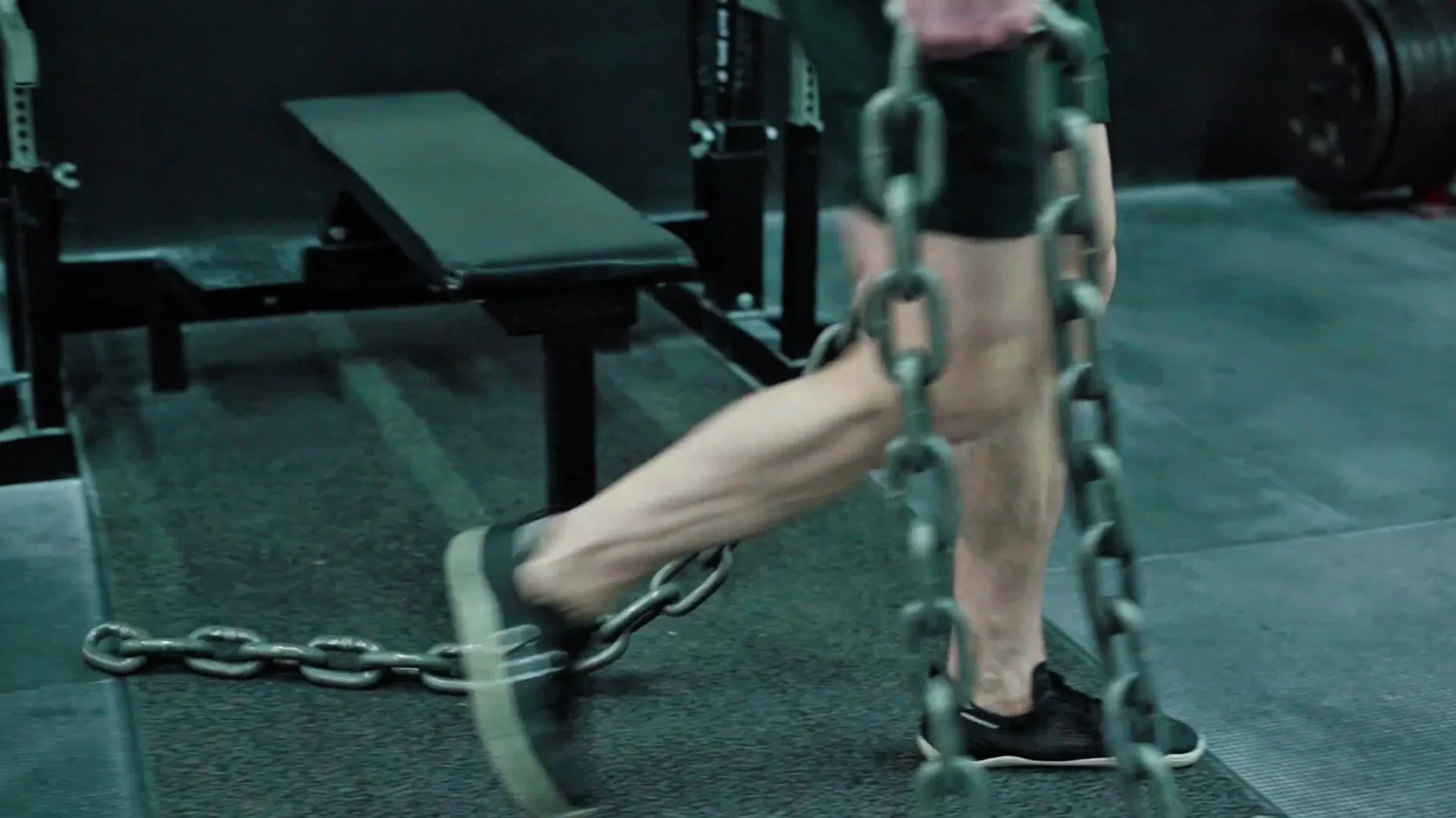 A loaded chain dragging across a dark gym floor beside an empty bench