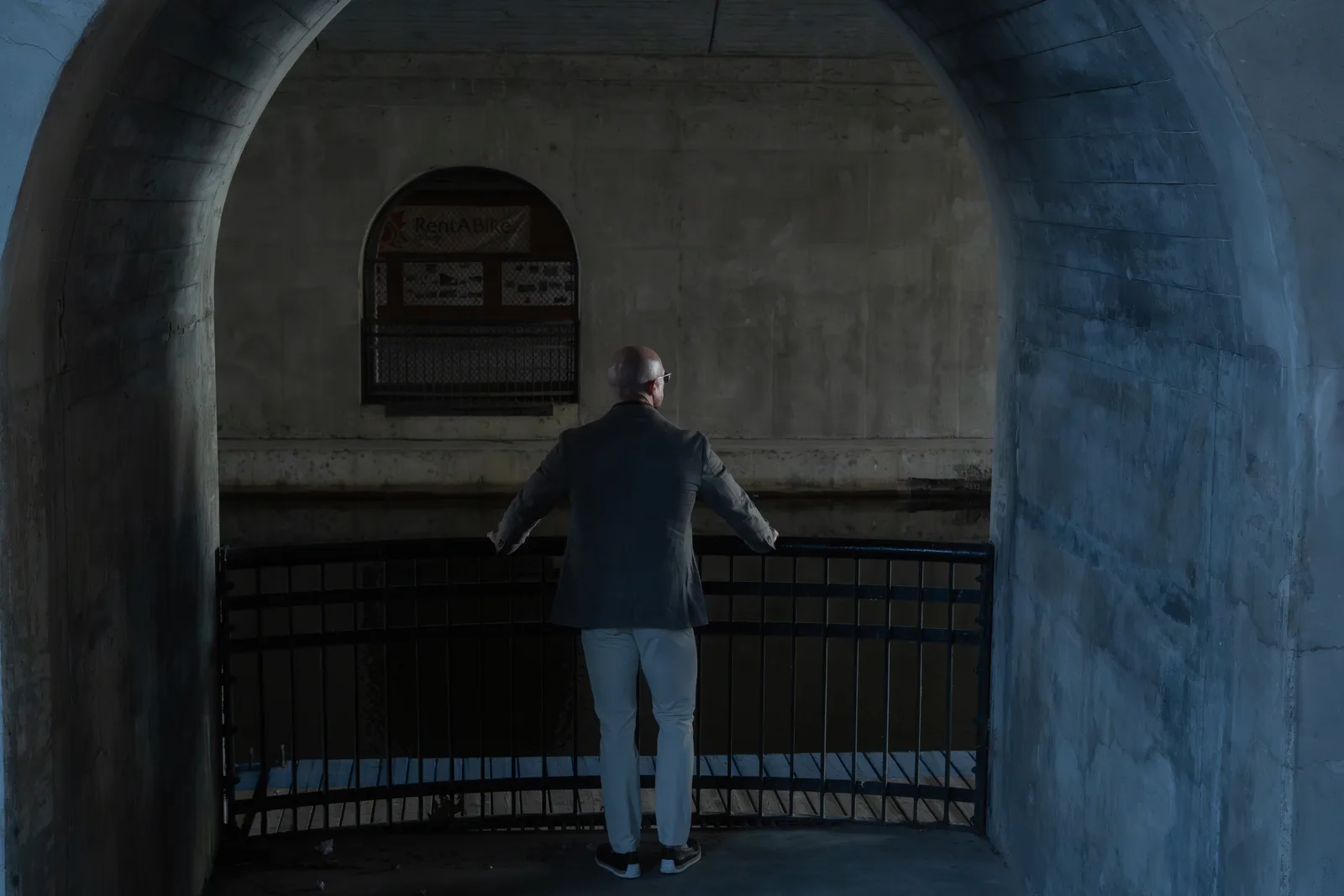 Tyson from behind, alone at a railing under a concrete arch