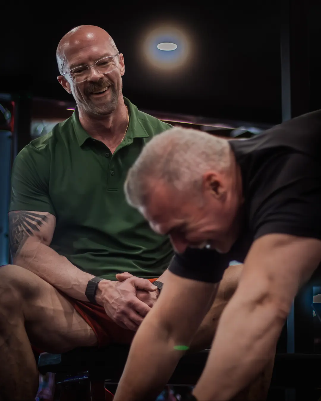 Tyson laughing beside a client working through a set in his gym.