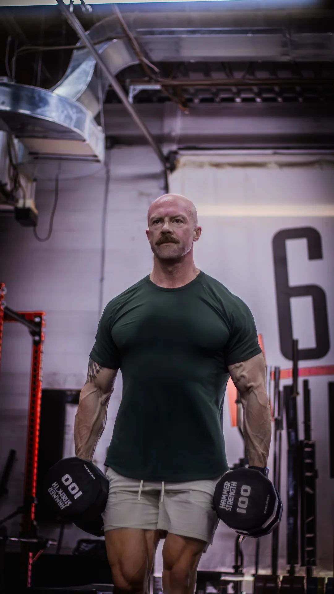 Tyson carrying a heavy dumbbell in each hand across his gym floor