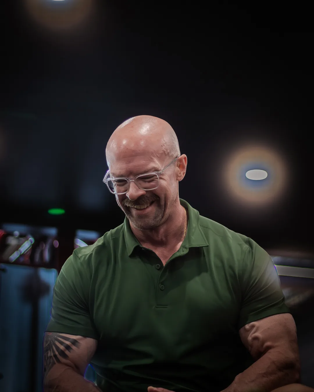 Tyson DesMarais between sets in his gym, head down and laughing, glasses catching the light.